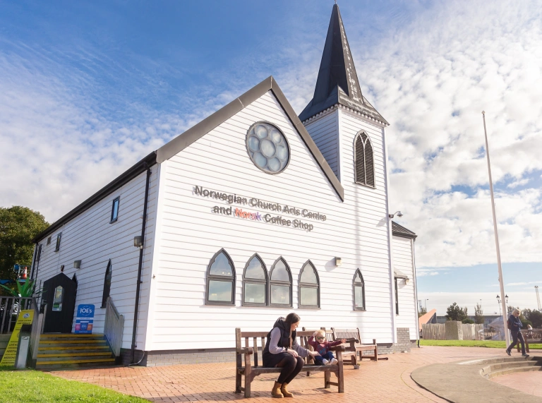 Eglwys wen gyda menyw a bachgen ifanc ar fainc y tu allan.