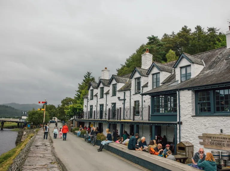 Hen dafarn, wedi’i phaentio’n wyn gyda balconi yn y ffrynt, gerllaw llwybr ar lan afon.
