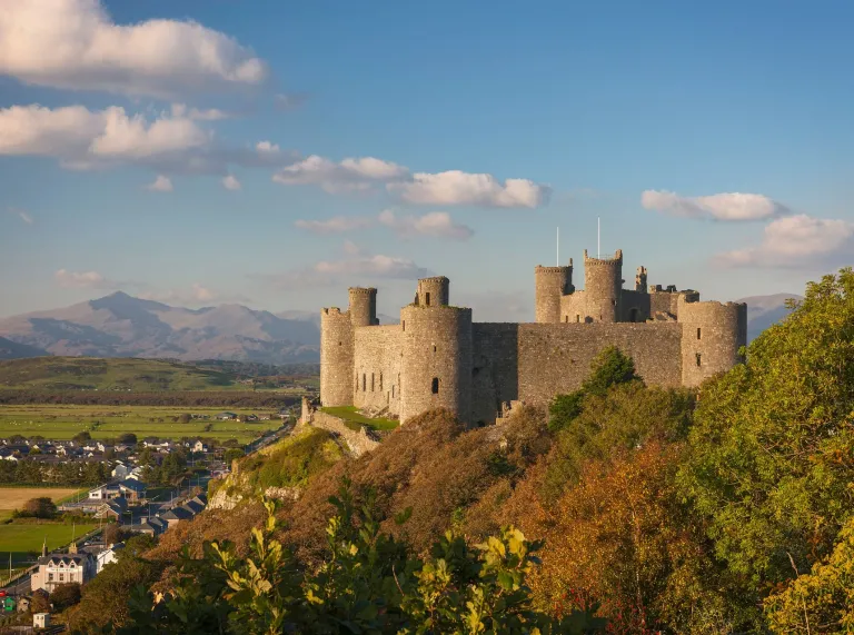 Castell yng nghesail bryn gyda mynyddoedd yn y cefndir.