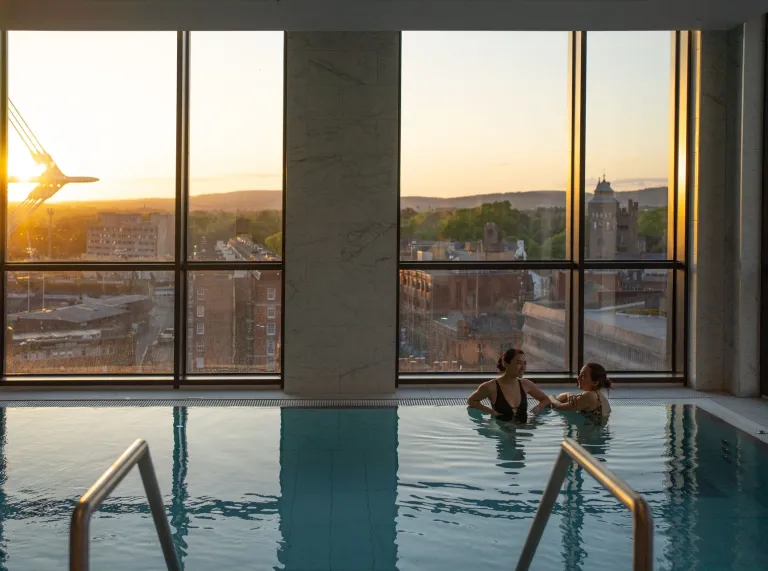 Two women in an indoor spa pool overlooking a city. 