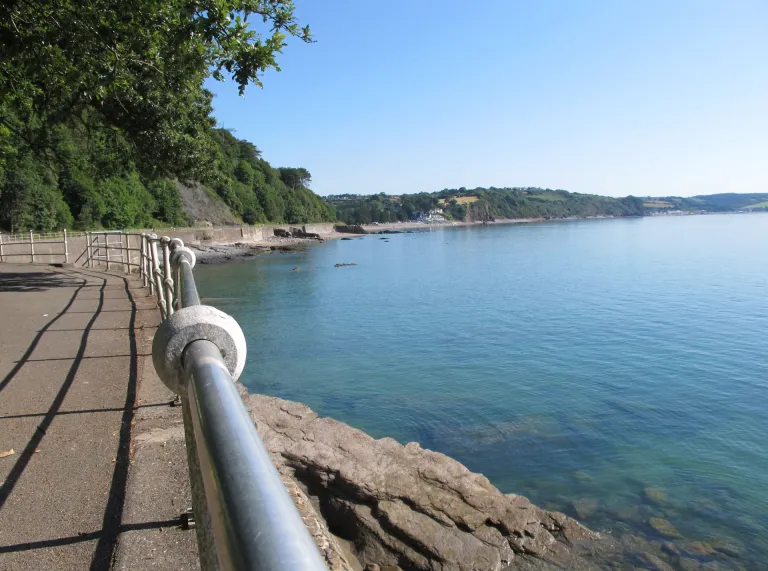 Llwybr arfordirol gyda rheiliau a môr ar ddiwrnod heulog.