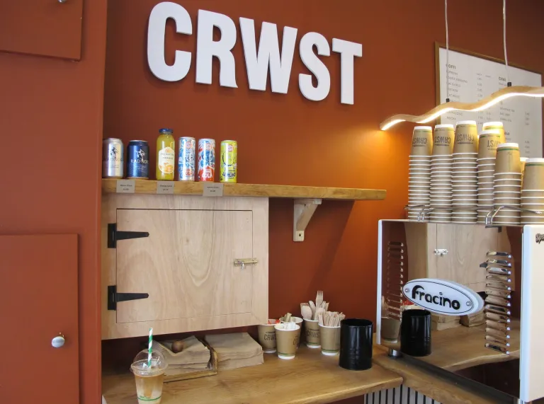 Cownter caffi gyda diodydd, pentwr o gwpanau gwag, peiriant, silff a chwpwrdd.