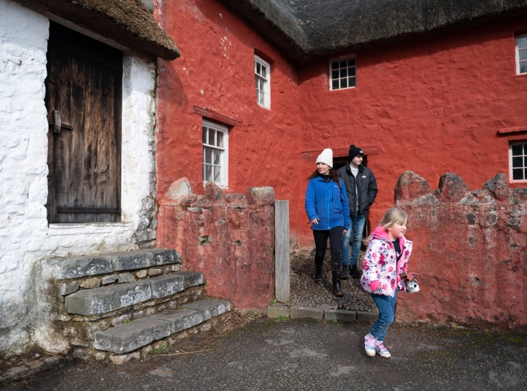 Oedolyn a dau o blant tu allan i ffermdy wedi ei baentio’n goch.