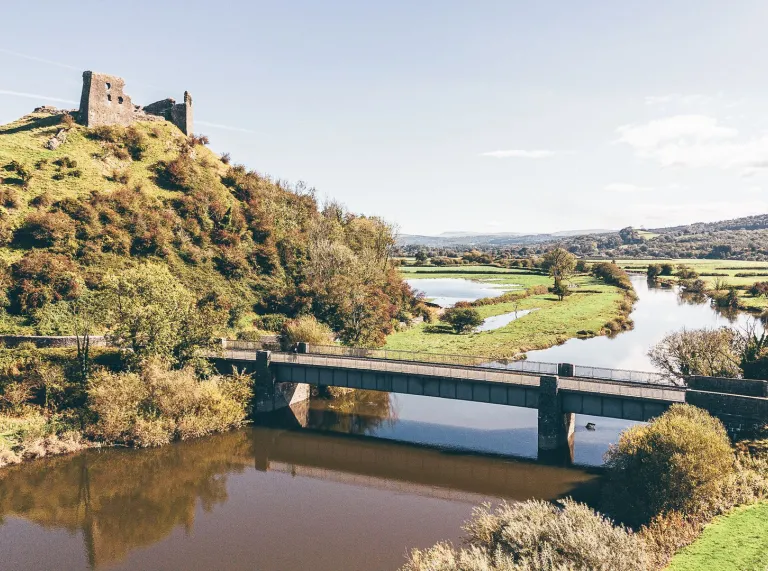 Castell adfeiliedig ar ben bryn sy'n edrych dros bont a dyffryn Afon Tywi.