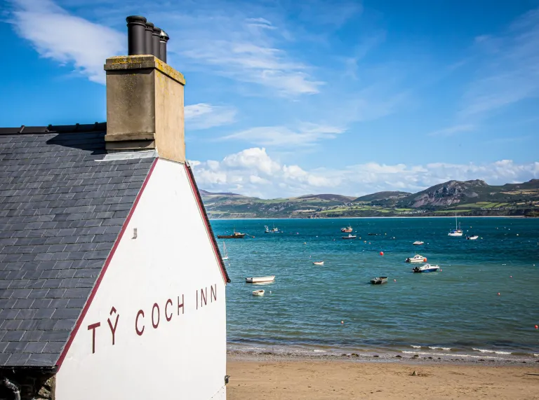 Bwthyn gwyngalch sy'n edrych dros fae tywodlyd gyda chychod a golygfeydd o'r môr.
