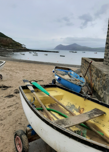 Cychod bach ar y traeth gyda'r môr yn y cefndir