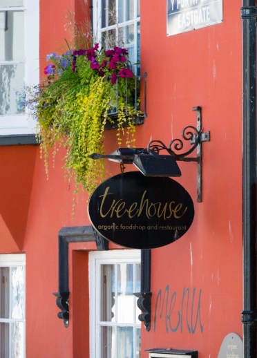 Arwydd du bwyty Treehouse ar adeilad oren gyda blodau ar y silff ffenestr allanol