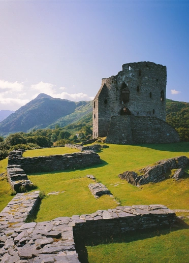Adfeilion castell gyda golygfa o fynyddoedd yn y cefndir