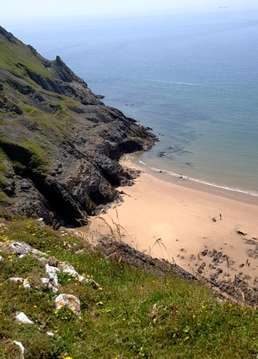 Golygfa o draeth gyda chlogwyni uchel a'r môr