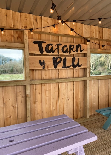 Tu fewn i dafarn mewn cwt pren gyda meinciau pren a goleuadau.