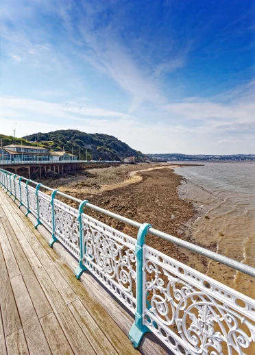 rhan o'r llwybr bwrdd a'r rheiliau pier, gyda golygfa o'r traeth a'r bryn yn y cefndir.