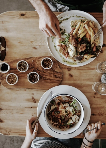 dwylo pobl a phlatiau ar fwrdd pren.