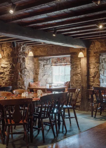 Ystafell fwyta draddodiadol yn y Blue Anchor Inn gyda waliau cerrig agored, trawstiau pren a byrddau a chadeiriau pren.