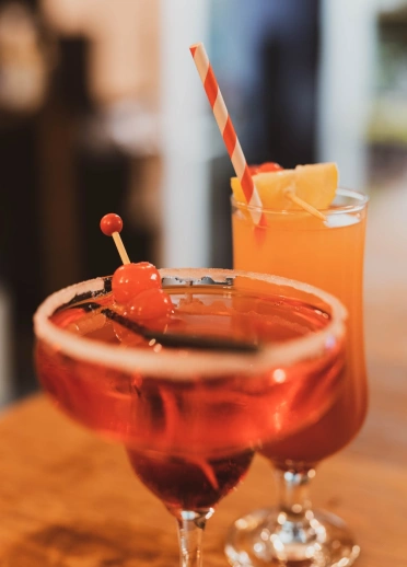 Coctel coch a choctel oren gyda gwelltyn a ffrwythau.