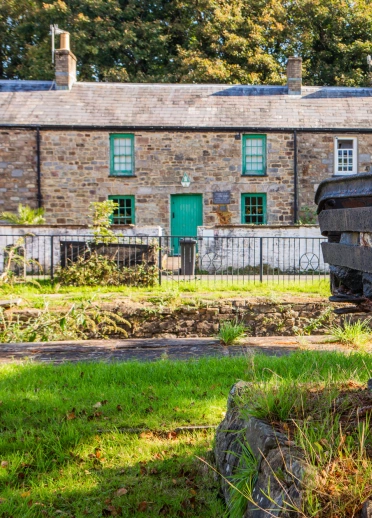 Golygfa allanol heulog o res o fythynnod carreg, gyda wagen lo dywyll o haearn a phren yn y blaendir.