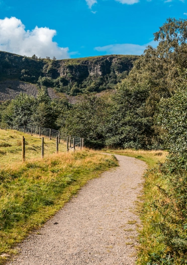 Llwybr cerdded o gwmpas cae gyda tharren werdd y tu cefn.