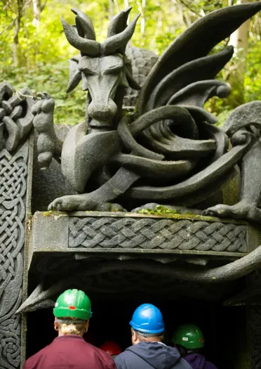 People wearing hard hats entering a cave with a large stone dragon above the entrance.