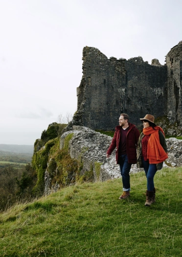 Pâr yn cerdded ger adfeilion castell yn yr hydref