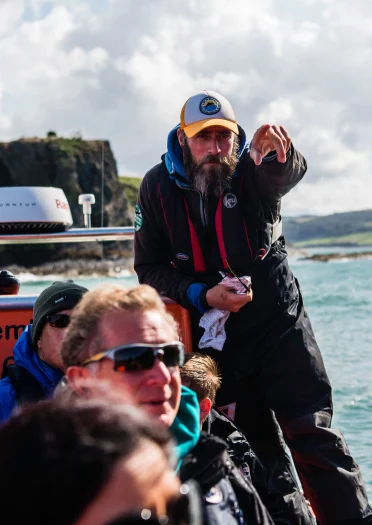 man stood pointing, with people sat on boat.