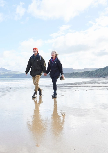 Cwpwl yn cerdded ar draeth Porthdinllaen