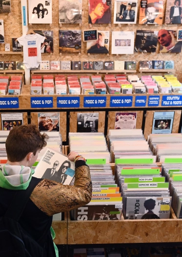 A man looking at a tray full of vinyl records inside a record shop.