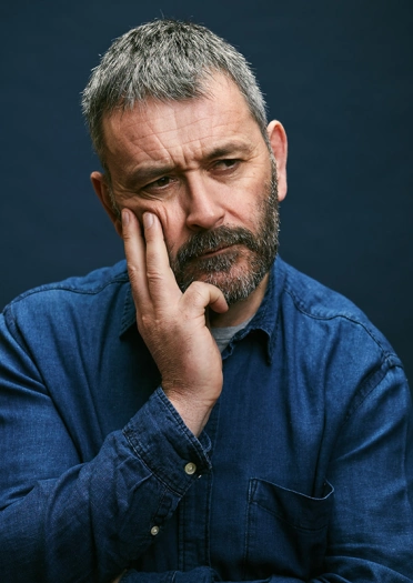 Llun o'r comediwr Tudur Owen yn edrych yn feddylgar