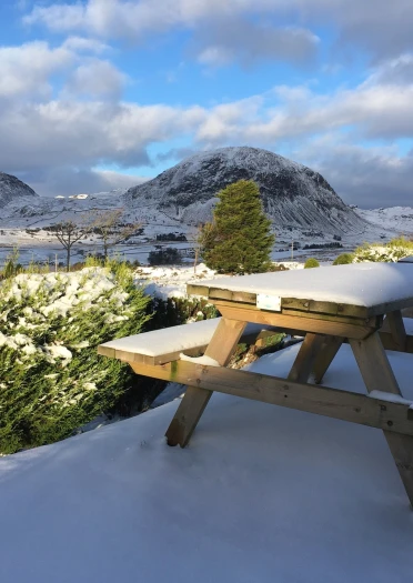 Seddi gardd dan eira â golygfeydd o fynydd dan eira.
