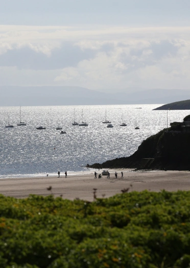 Llun o'r traeth gyda'r môr a chychod bach yn y pellter