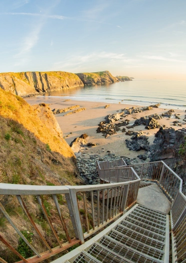 Grisiau metel serth i lawr i’r traeth.