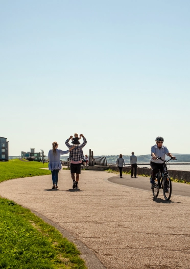 people walking and cycling along coastal walkway.