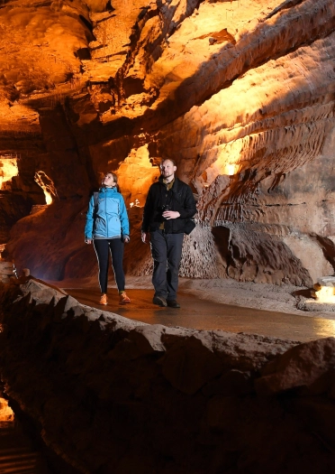 Dwy bobol yn cerdded trwy ogof gyda goleuadau