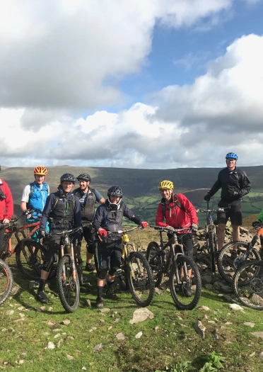 Grŵp mawr o feicwyr mynydd ar ben bryn.