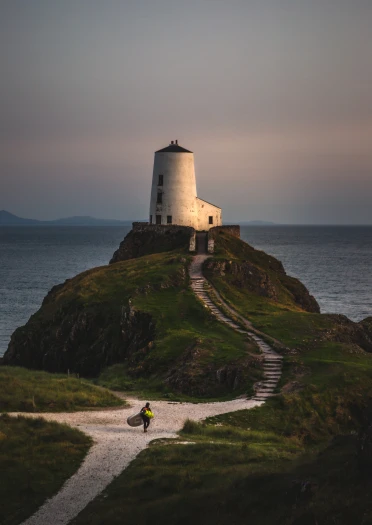 Golygfa o Ynys Llanddwyn gyda chlogwyn a môr a pherson yn cario padlfwrdd