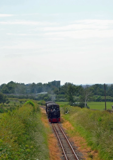 Tren ar drac gyda'r arfordir yn y cefndir.