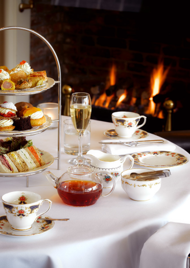 Bwrdd ac arno de prynhawn, potel siampên a thân yn y cefndir.