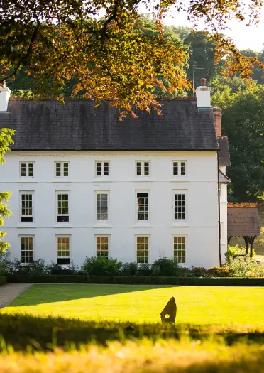 tu allan i adeilad gwyn wedi ei amgylchynu gan goed.