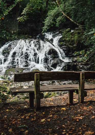 Wooden bench in front of waterfall. Mainc bren o flaen y rhaeadr.