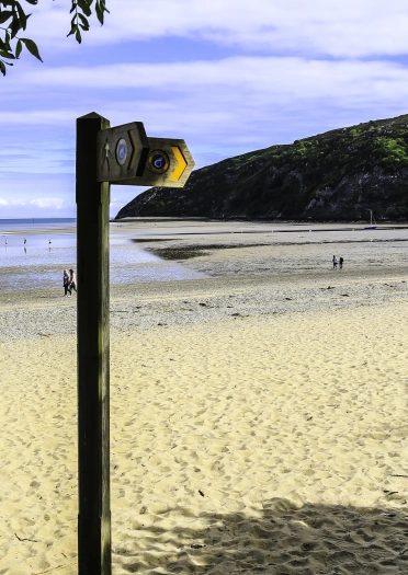 Arwydd pren ar gyfer Llwybr Arfordir Cymru ar draeth tywodlyd.