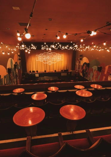 Inside a cinema with round tables in front of traditional cinema seats.