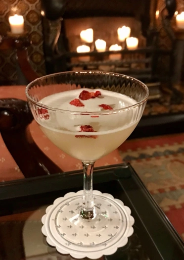 Coctel gin ar fwrdd, o flaen tân yn llawn canhwyllau mawr.