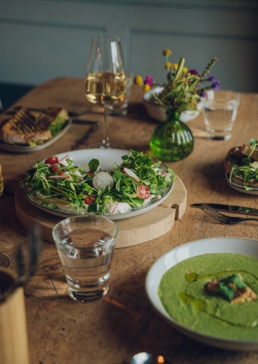 Prydau bwyd - cawl gwyrdd a phlatiad o salad - ar fwrdd pren. Mae gwin a dŵr ar y bwrdd hefyd.