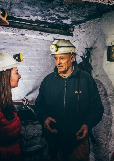 Pedwar o oedolion yn gwisgo oferôls a helmedi caled gyda fflachlampau ar eu blaen.