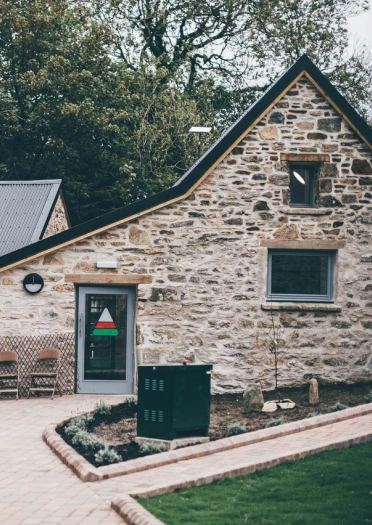 Adeiladau cerrig gyda gardd o'u blaenau. Mae logo triongl coch gwyn a gwyrdd yr Urdd o'u blaen.
