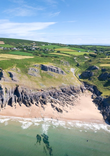 Llun o’r awyr o draeth creigiog mewn cildraeth rhwng clogwyni.