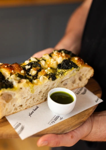 dyn yn dal bara focaccia fegan a hufen.