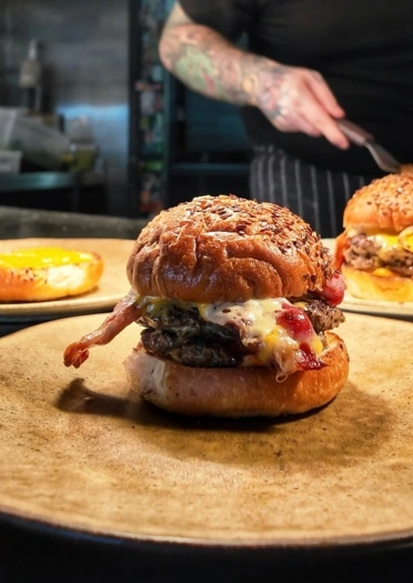 burgers on wooden platters with tattooed arm in background.
