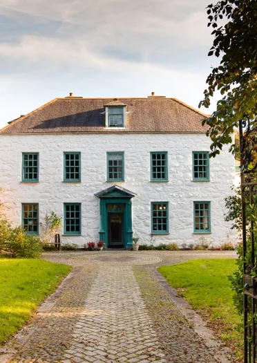 Llun o'r tu allan i dŷ mawr gwyn gyda llwybr a gatiau ar agor yn y tu blaen