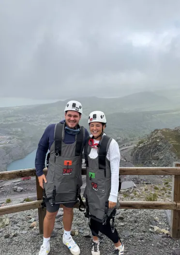 Dau o bobl yn gwisgo helmedi gyda chwarel yn y cefndir.