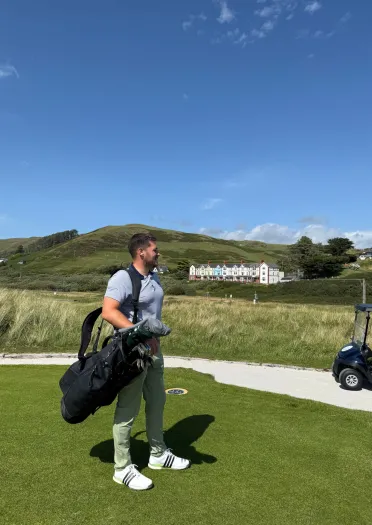 Dyn yn gafael mewn bag golff ar gwrs golff.