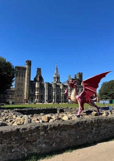 Cerflun o ddraig ar wal isel, gydag adeilad yn y cefndir.